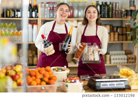 Young saleswomen are holding champagne, wine and sweets in their hands. 133012198