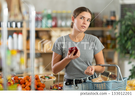 Young woman with phone choosing groceries in store 133012201