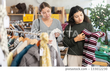 Latin woman with female companion is busy looking at clothes items, choose winter sweater Latin woman with female companion is busy looking at clothes items, choose winter sweater 133012230