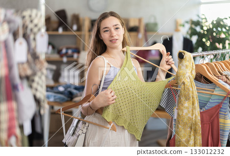 Positive young woman choosing something for summer in clothing store 133012232