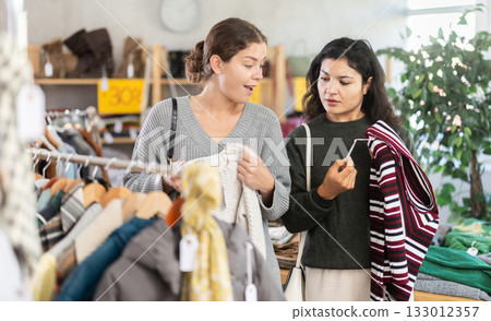 Two women choosing warm sweaters in a store with clothes in the background 133012357