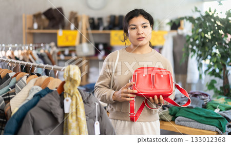 Happy latina woman standing in interior of clothing boutique and choosing fashionable handbag. Winter collection sale 133012368