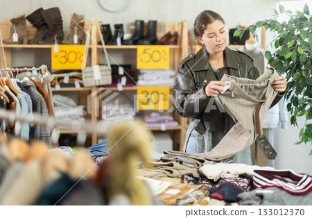In sales area of store, woman customer chooses trousers 133012370