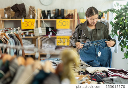 In sales area of store, woman customer chooses trousers 133012378