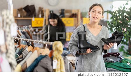 European woman chooses boots with heels and black shoes in the store 133012397