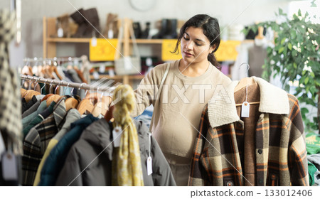 Pregnant Latina holding hangers with jackets Pregnant Latina holding hangers with jackets 133012406