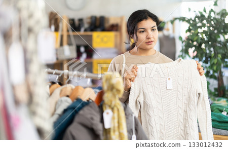 Positive latina young woman shopping sweaters in store. Sale of winter clothing collection 133012432