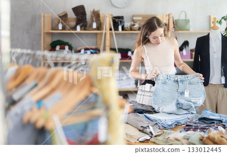 Search and selection of new jeans or shorts in clothing store for woman 133012445