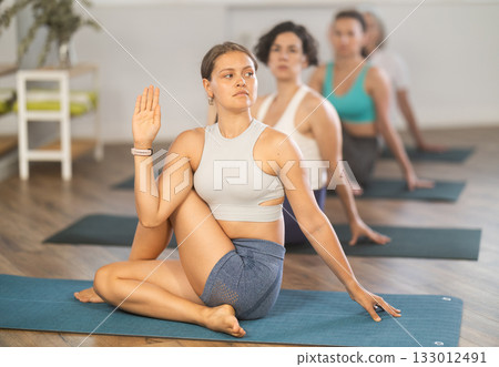 Girl performing Matsyendrasana twisting asana in yoga studio Girl performing Matsyendrasana twisting asana in yoga studio 133012491