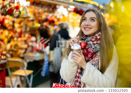 Girl with ball for Christmas tree in her hands stands in middle of New Year market 133012505
