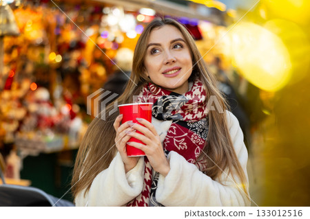 Young woman stands with glass of hot coffee in her hands and enjoys festive New Year atmosphere Young woman stands with glass of hot coffee in her hands and enjoys festive New Year atmosphere 133012516