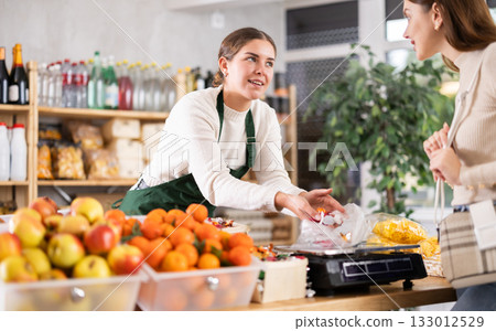 Woman sells and puts candies in bag for young woman, puts them on scale and weighs fruits Woman sells and puts candies in bag for young woman, puts them on scale and weighs fruits 133012529