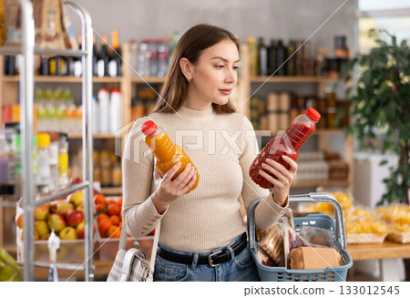 Young woman choosing juices in grocery store 133012545