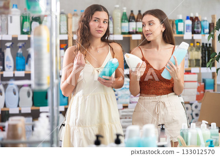 Two girlfriends buyer chooses shampoo or shower gel in household goods department of supermarket 133012570