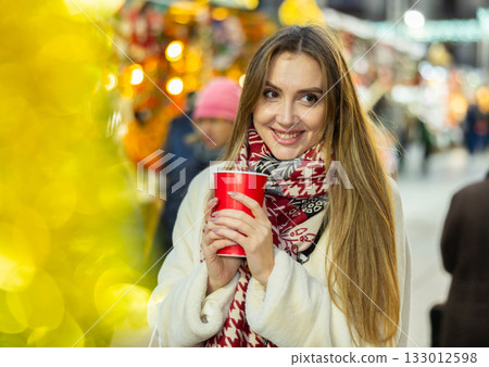 Young woman stands with glass of hot coffee in her hands and enjoys festive New Year atmosphere Young woman stands with glass of hot coffee in her hands and enjoys festive New Year atmosphere 133012598