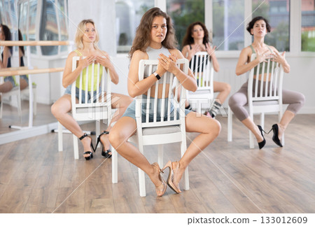 Group of women in high heels rehearsing dance while sitting on chair Group of women in high heels rehearsing dance while sitting on chair 133012609