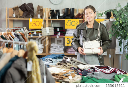 Girl is busy looking at clothes items in store, she chooses handbag Girl is busy looking at clothes items in store, she chooses handbag 133012611
