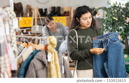 Latin girl is busy looking at clothes items in store, she chooses jeans 133012615