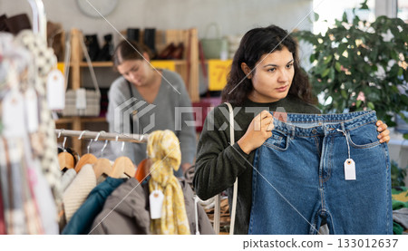 Latin girl is busy looking at clothes items in store, she chooses jeans 133012637