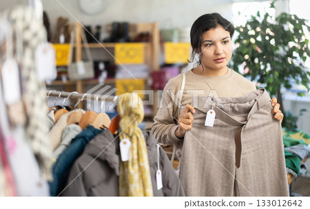 Focused latina young female client choosing pants or stylish trousers in clothing mall 133012642