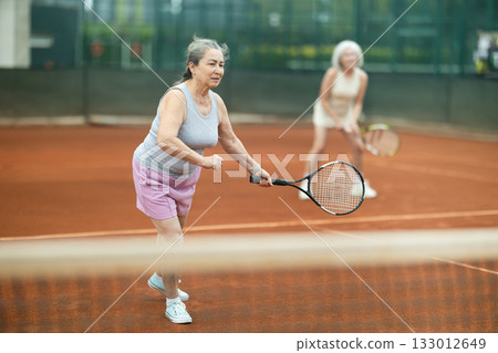Elderly woman engrossed in doubles tennis game on clay court Elderly woman engrossed in doubles tennis game on clay court 133012649