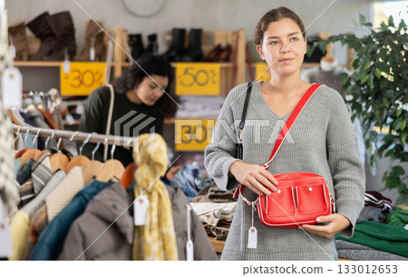 Girl is busy looking at clothes items in store, she chooses handbag 133012653