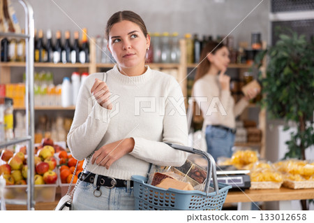 Portrait of girl shopper with a shopping cart choosing some products in supermarket 133012658