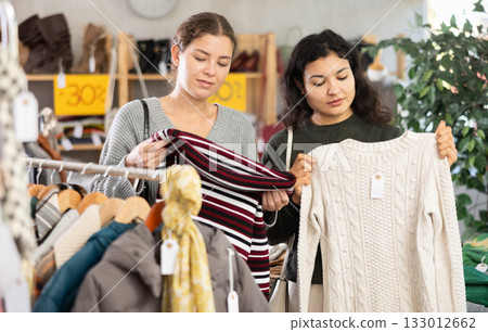 Latin woman with female companion is busy looking at clothes items, choose winter sweater 133012662