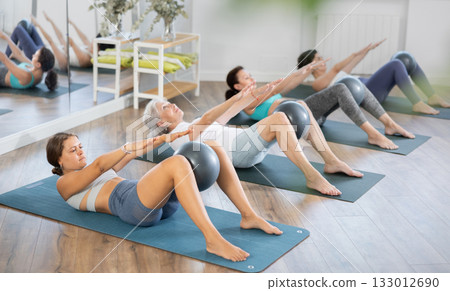 Female Pilates instructor doing Half Roll Back with ball at group training 133012690