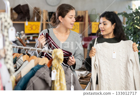 Two focused female clients carefully looking sweaters for autumn-winter season in clothing mall 133012717