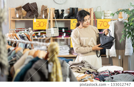 Latin girl is busy looking at clothes items in store, she chooses handbag 133012747