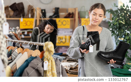 Girl is busy looking at clothes items in store, she chooses winter coat or jacket 133012767
