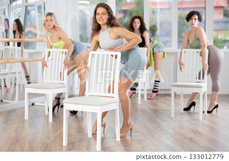 Young woman stands next to chair, leans on back and performs set of lap dance movements 133012779