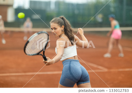 Sporty young girl playing doubles tennis on outdoor court Sporty young girl playing doubles tennis on outdoor court 133012783