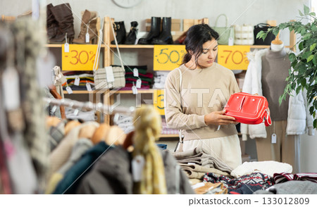 Happy latina woman standing in interior of clothing boutique and choosing fashionable handbag. Winter collection sale 133012809