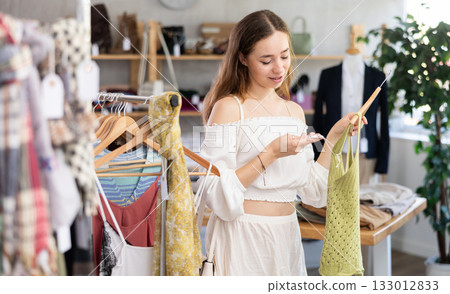 Positive joyful woman looking for fashionable clothes in clothing boutique 133012833