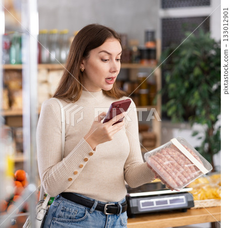 Young woman scanning qr code of raw sausages Young woman scanning qr code of raw sausages 133012901