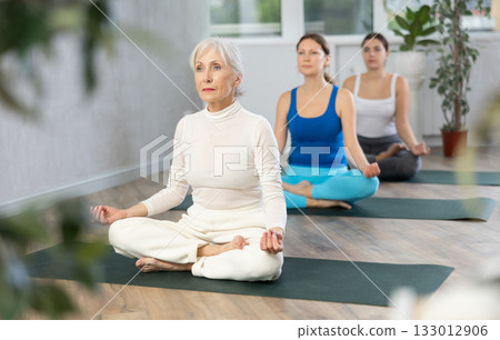 Senior woman sitting in Padmasana yoga position with hands in mudra 133012906