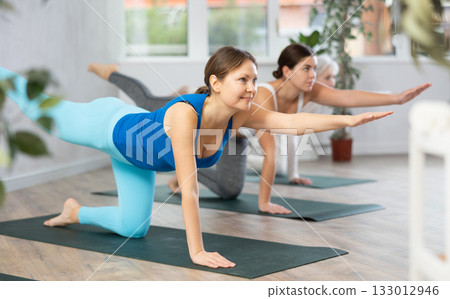 Woman doing yoga with group in fitness studio, standing in stretching asana Mukha Shvanasana Woman doing yoga with group in fitness studio, standing in stretching asana Mukha Shvanasana 133012946
