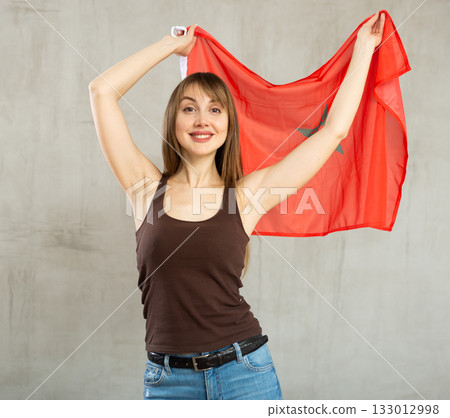 Smiling woman waving Moroccan flag against gray background Smiling woman waving Moroccan flag against gray background 133012998