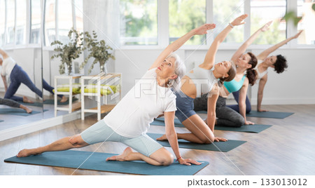 Senior woman performing Gate Pose during group yoga practice Senior woman performing Gate Pose during group yoga practice 133013012