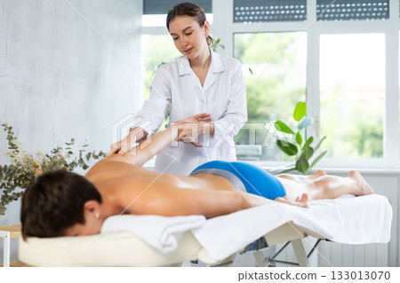 Professional young masseuse performing back massage for male patient Professional young masseuse performing back massage for male patient 133013070