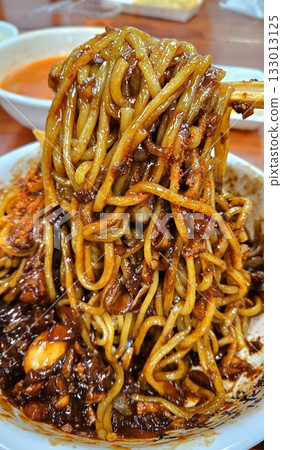 Classic jajangmyeon with thick noodles in a rich black bean sauce, garnished with sliced cucumber and sesame seeds. A beloved Korean-Chinese comfort dish, full of savory depth and flavor. 133013125