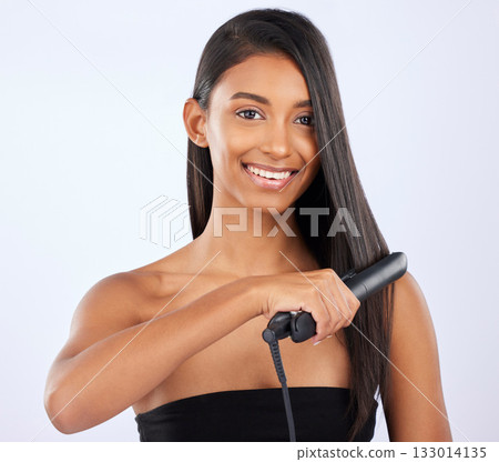 Haircare, beauty and woman with a straightener in studio for a straight, long and healthy hairstyle. Happy, smile and portrait of a female model with flat iron after hair treatment by gray background 133014135