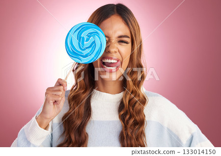 Portrait, funny face and lollipop with a woman in studio on a pink background holding giant candy. Comic, comedy and sweet with a playful young female feeling silly while eating a blue sugar treat 133014150