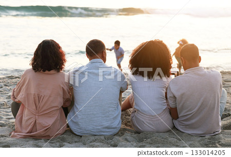 Family sitting on beach from the back, sunset and view of waves, zen and children playing in water together. Holiday, men and women relax in peace at evening ocean in Indonesia on tropical vacation. Family sitting on beach from the back, sunset and view of waves, zen and children playing in water together. Holiday, men and women relax in peace at evening ocean in Indonesia on tropical vacation. 133014205