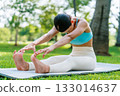 Young Asian woman doing yoga stretching on green grass with trees in the background on a sunny day 133014637