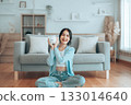 Young Asian woman holding piggy bank and sitting on the floor at home 133014640
