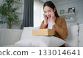 Happy young Asian woman opening delivery package at home 133014641