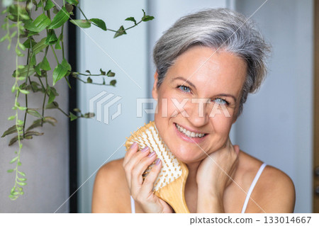 Portrait of a beautiful gray-haired European woman with a wooden comb. Mirror in the bathroom Portrait of a beautiful gray-haired European woman with a wooden comb. Mirror in the bathroom 133014667
